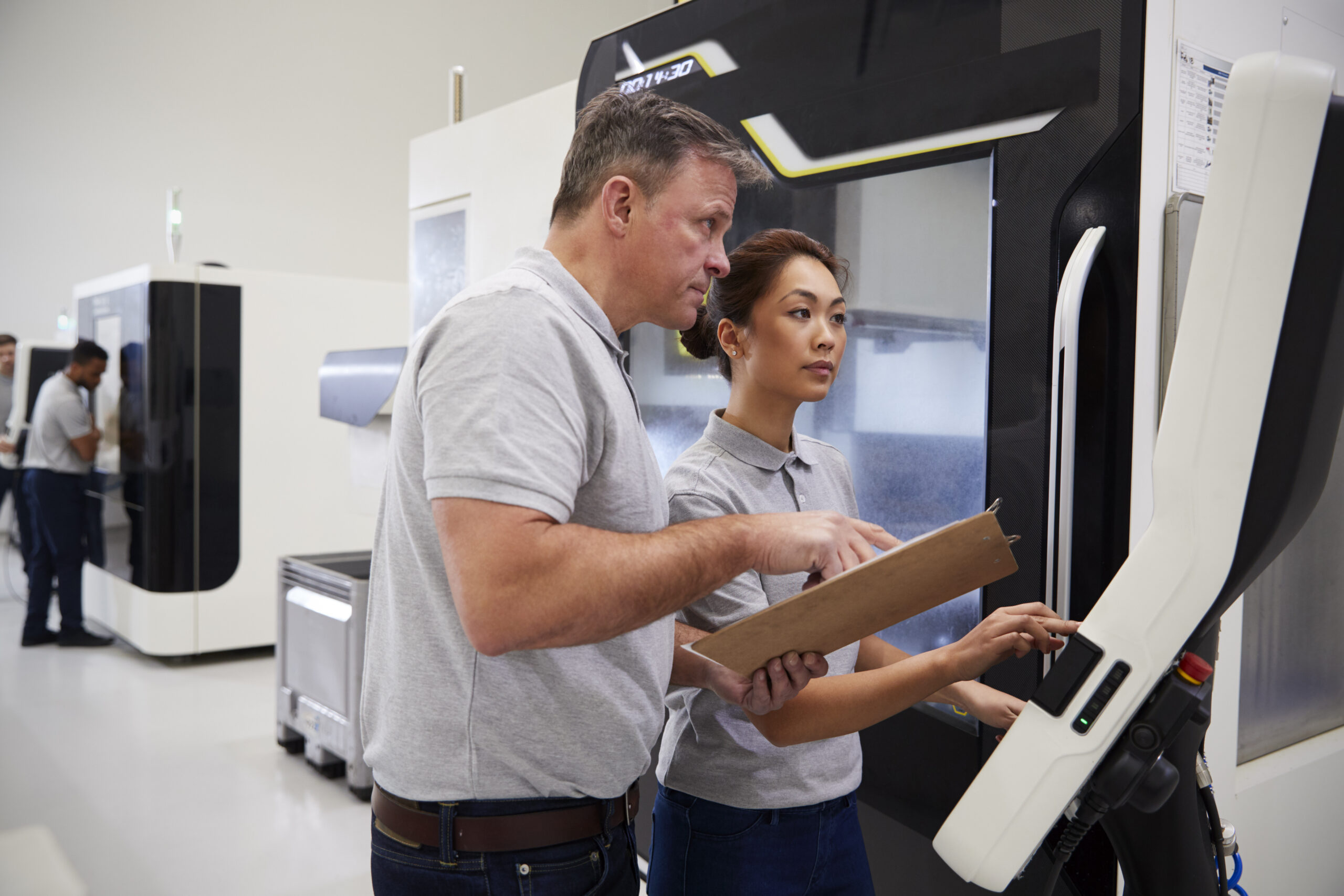 Engineer training female apprentice to use a CNC machine in a factory