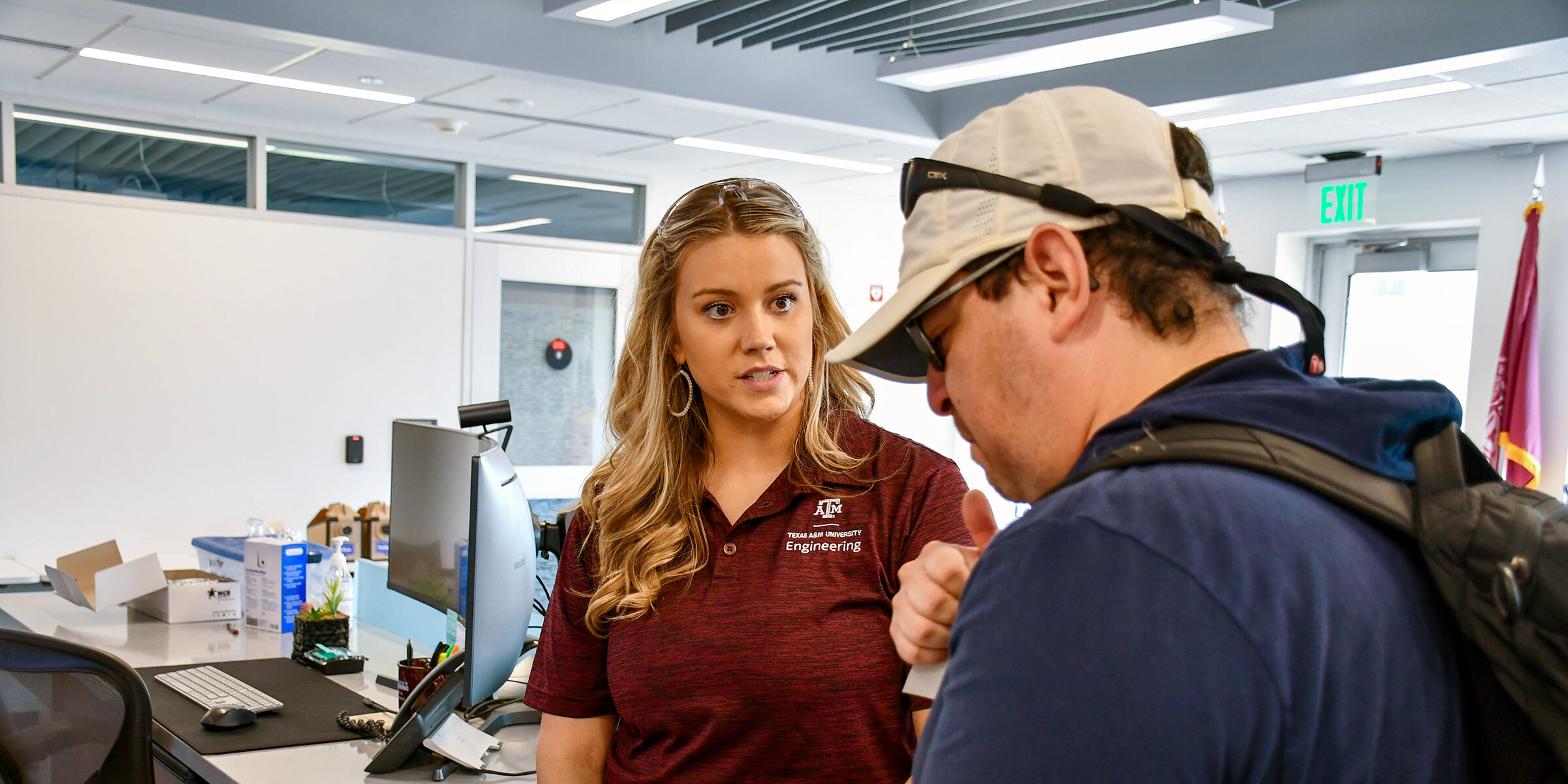 A female organizer discussing a flyer for the Project MFG Additive Competition with a male student.
